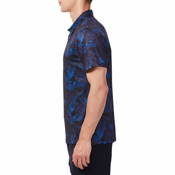 Men's Short sleeve polo shirt in a blue and black allover palm frond print.Has a 3 button front colosure and pointed blue collar made from knit fabric on a model - side view