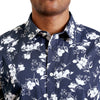 close up view of the pointed collar and neck area of cotton fabric button up shirt in a white floral pattern on navy ground. Worn by a black male model. The top buttons are undone