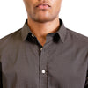 close up view of the pointed collar and neck area of cotton fabric button up shirt in a tan and white pattern on black ground. Worn by a black male model. The top buttons are undone